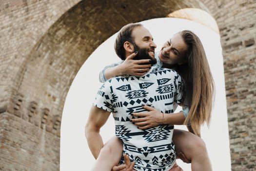 Caucasian man carry smiling woman against the background of viaduct, middle-aged couple enjoying weekend outdoors