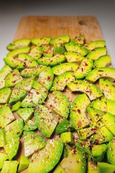 Avocado slices on a wooden textured background sprinkled with spices, bright accent. View from above.
