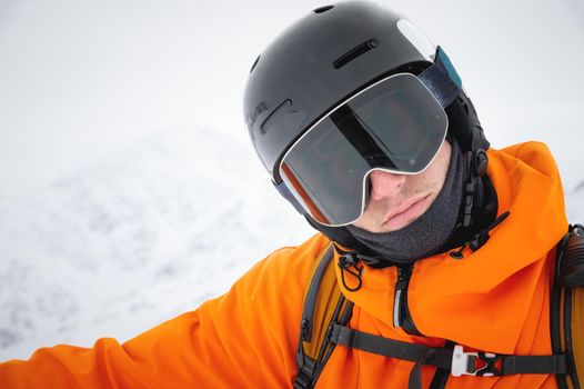 Close-up of a man's ski goggles looking straight into the camera. Portrait of a man in a ski resort against the backdrop of mountains and sky.