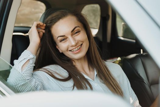 Middle aged woman with dental braces smiling while sitting inside the car