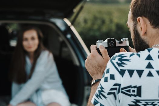 Man using old film camera to photography his girlfriend who sitting inside trunk of car