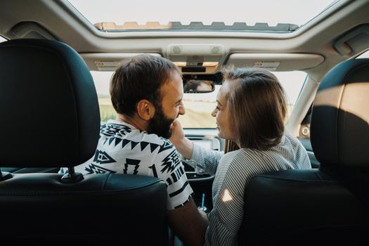 Happy middle-aged couple enjoying road trip together, cheerful caucasian man and woman sitting inside SUV car while on vacation