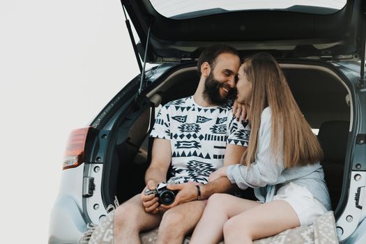 Middle-aged couple sitting in trunk of car and smiling, caucasian man and woman enjoying road trip