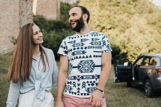 Happy middle-aged couple walking outdoors, caucasian man and woman enjoy road trip on SUV car