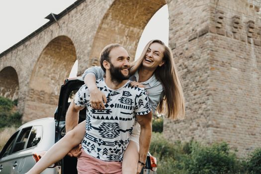 Caucasian man carry smiling woman against the background of viaduct, middle-aged couple enjoying roadtrip. High quality photo