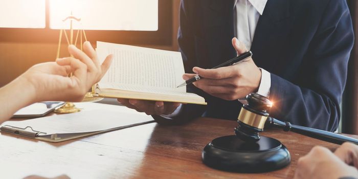 Lawyer hands holding a legal book and clarify the law to client while sign a contract at lawyer office.