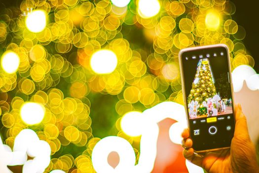 hand holding mobile smart phone with Christmas light decorated background