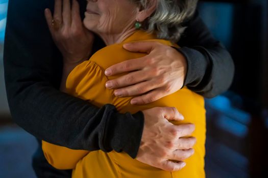 A young girl happily hugs her grandmother in a cozy house against the backdrop of the kitchen, her daughter has a good time with her mother, lovingly cares for and supports an elderly relative.