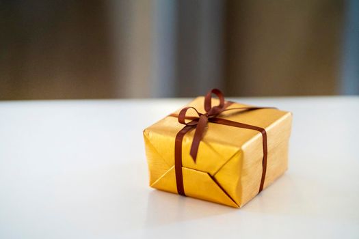 A cute little gift in a golden wrapper and with a ribbon lies on the table, a beautiful surprise for the holidays