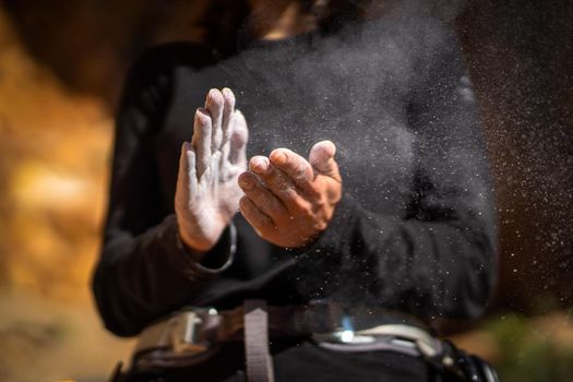 The girl is engaged in rock climbing, uses white powder of magnesia, claps her hands close-up, the woman leads an active lifestyle, climbs the mountains outdoor.
