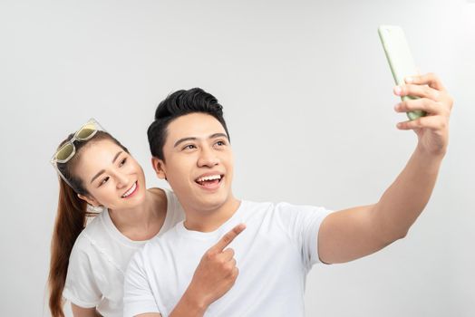 selective focus of happy asian couple taking selfie on smartphone isolated on white