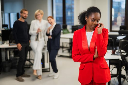 Young african woman crying because of the ridicule of colleagues. Racial discrimination in the office