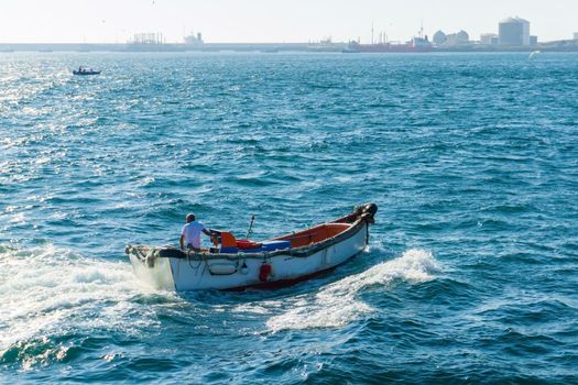 A fisherman on an old motor boat returns to the harbor on a sunny day