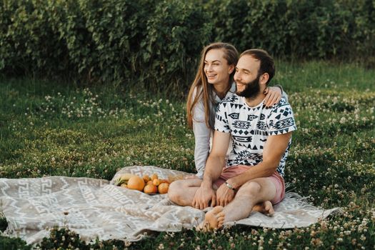 Cheerful man and caucasian woman sitting on blanket and enjoying weekend picnic together, happy middle-aged couple having picnic outside city