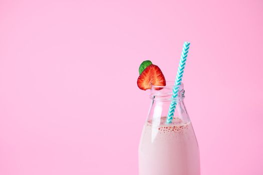 Close-up strawberry smoothie or milkshake in glass jar with berries on pink background. Healthy summer drink