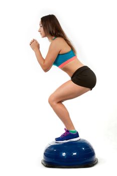 Young sports girl does exercises squatting on spotrivnom simulator bosu. Portrait in full growth. View profile.