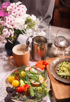 Kitchen garden vegetables on plate with bread, herbs and edible flowers, nasturtium and borage, a cup of coffe with milk on white table, summer breakfast concept, selective focus.