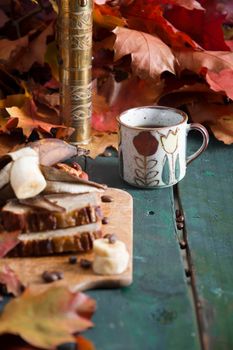 Banana pie on a background of autumn bright leaves, a copper coffee grinder and a ceramic cup with coffee on a wooden background. High quality photo