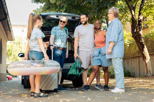 Mixed family and friends going on vacation at seaside, travelling by car with luggage and suitcase. Child, parents and grandparents leaving on summer holiday trip with baggage and inflatable.