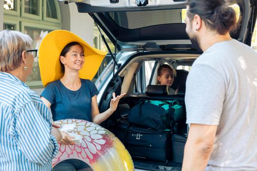 Happy family travelling on seaside vacation, leaving with suitcase and baggage in car trunk. Little girl, parents and grandparents going to sea destination with automobile, to travel on holiday.