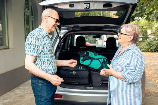 Old husband and wife travelling on vacation, using car for road trip journey with suitcase and baggage. Going on retirement holiday with luggage and travel bags, leaving house during summer.