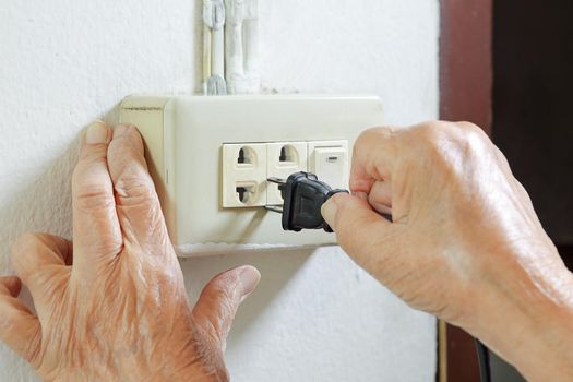 Elderly woman trying plug cable to the electric outlet
