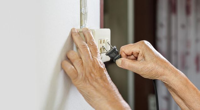 Elderly woman trying plug cable to the electric outlet