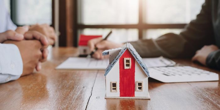 Miniature of cottage house on table close up view, happy African family, agency or bank clients handshake real estate agent after contract signing.