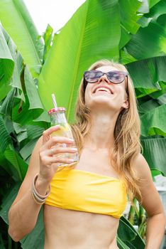 Summer vacation. Beautiful woman in yellow swimsuit and sunglasses with long hair and palm leaves. Beautiful caucasian girl in stylish swimwear in tropical nature