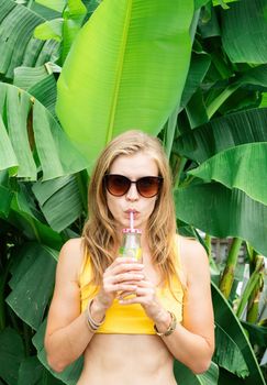 Summer vacation. Beautiful woman in yellow swimsuit and sunglasses with long hair and palm leaves. Beautiful caucasian girl in stylish swimwear in tropical nature