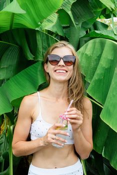 Summer vacation. Beautiful woman in white swimsuit with long hair and palm leaves. Beautiful caucasian girl in stylish swimwear in tropical nature