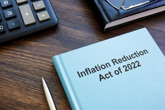 Blue book with The Inflation Reduction Act of 2022 near calculator and notebook.