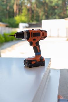 Cordless screwdriver stands on a wooden panel. A wireless tool for working outdoors in the absence of an electrical network.
