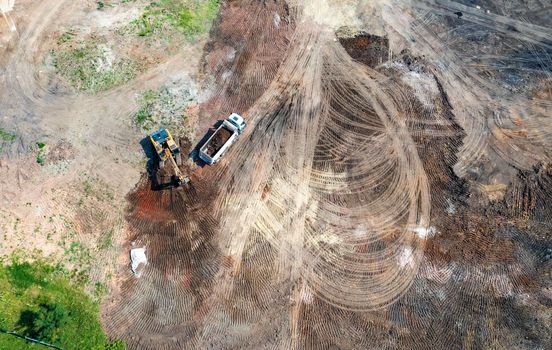 Aerial top view of excavator and dump trucks working at the construction site