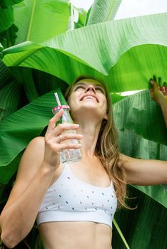 Summer vacation. Beautiful woman in white swimsuit with long hair and palm leaves. Beautiful caucasian girl in stylish swimwear in tropical nature