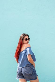 Attractive young woman in summer clothes and sunglasses, dancing on blue wall background at street