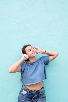 Attractive young woman in summer clothes and sunglasses listening to the music on blue wall background at street