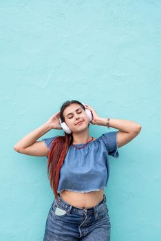 Attractive young woman in summer clothes and sunglasses listening to the music on blue wall background at street