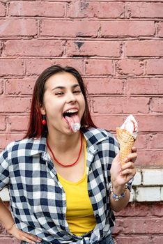 Attractive young woman in summer clothes and sunglasseseating ice cream on pink brick wall background at street