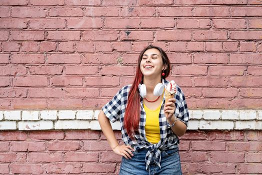 Attractive young woman in summer clothes and sunglasseseating ice cream on pink brick wall background at street