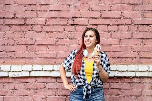 Attractive young woman in summer clothes and sunglasseseating ice cream on pink brick wall background at street