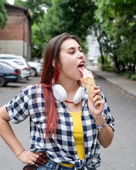 Attractive young woman in summer clothes and headphones eating ice cream at street