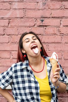 Attractive young woman in summer clothes and sunglasseseating ice cream on pink brick wall background at street