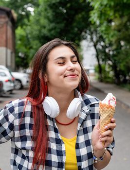 Attractive young woman in summer clothes and headphones eating ice cream at street