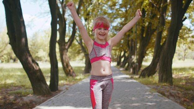 Athletic fitness sport runner child girl finishing racing competition. Victory and success. Workout cardio training in park. Toddler kid jogger champion winning marathon. Active children motivation