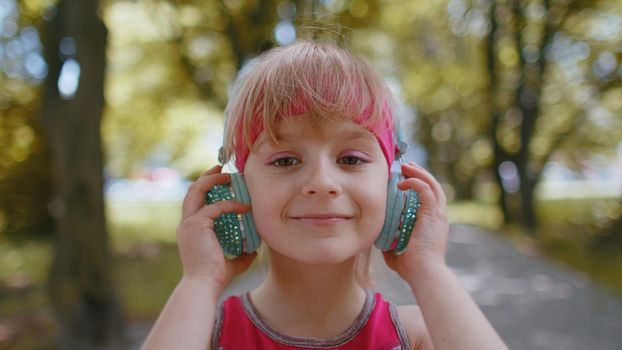 Close up of athletic fitness sport runner child girl wearing headphones listening favorite music song. Workout training cardio in park. Toddler kid jogger enjoy healthy lifestyle. Active children