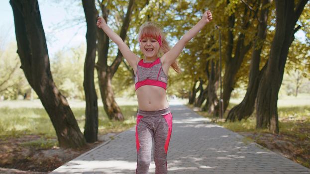 Athletic fitness sport runner child girl finishing racing competition, victory. Celebrating, dancing. Workout cardio training in park. Toddler kid jogger champion winning marathon. Children motivation