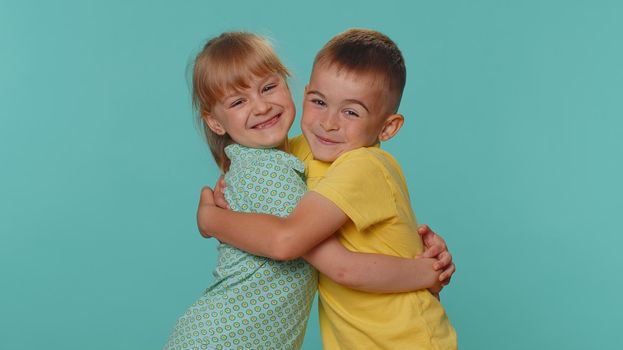 Cheerful funny little toddler children boy girl siblings or friends smiling, looking at camera, enjoying success, surprise. Young preschool kids embracing hugging isolated on blue studio background
