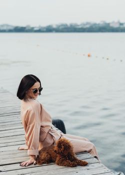 Brunette woman sitting on the pier with her redhead dog toy poodle