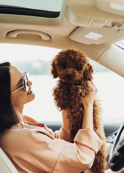 Young brunette woman happy owner of redhead dog toy poodle, adult girl sitting inside car with her four paws pet